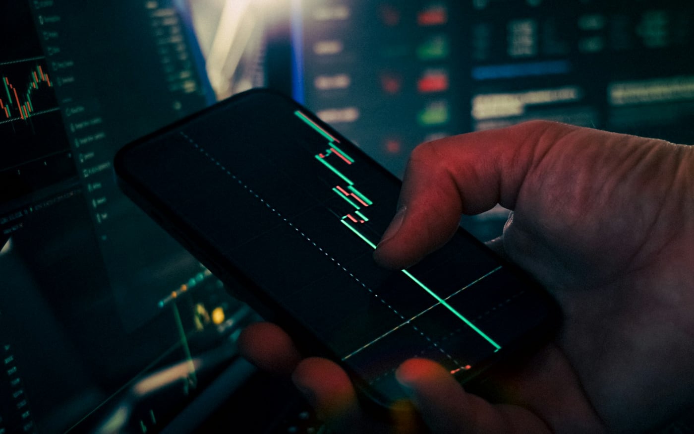 Člověk sleduje tržní grafy na telefonu jako symbol rozdílu mezi investováním a spekulací.